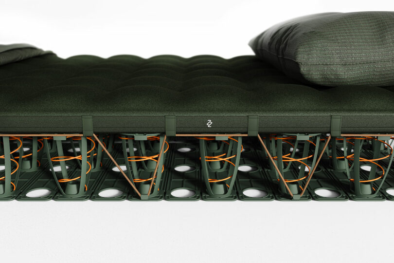 A close-up side view of a mattress with visible springs and support structure beneath a green cushioned top and pillows.