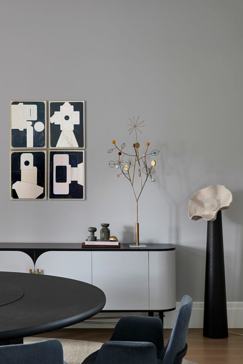 A modern living room with abstract art on the wall, a decorative gold sculpture, books, and a white console table; a tall sculptural piece stands on the right.