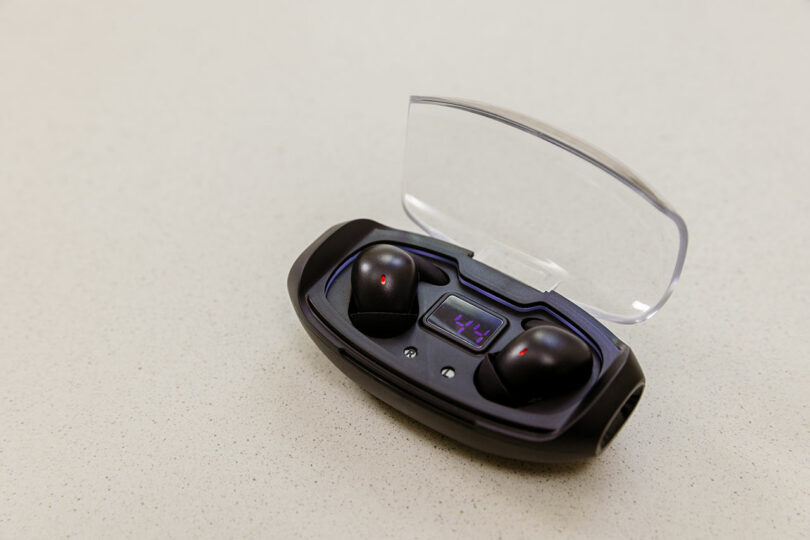 SleePods: A pair of black wireless earbuds in a charging case with a transparent lid, displaying a digital charge percentage.