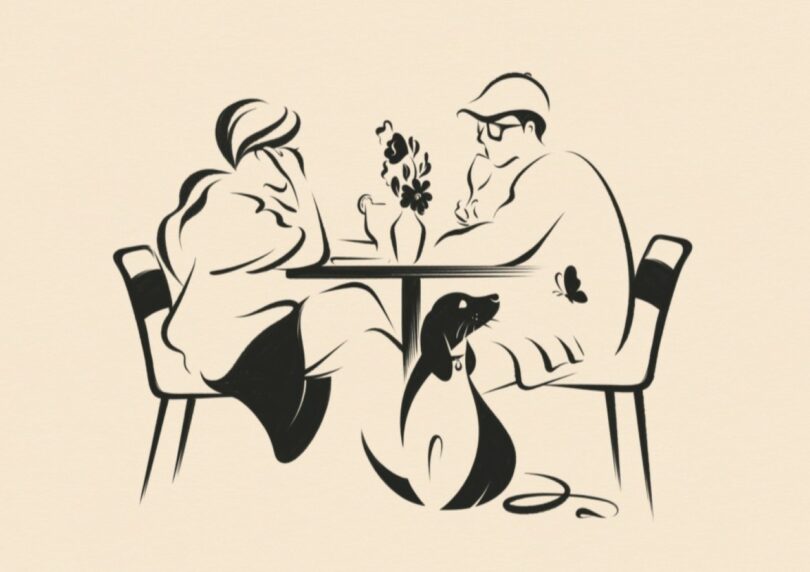 A man and woman sit across from each other at a table with flowers, while a dog sits on the floor between them