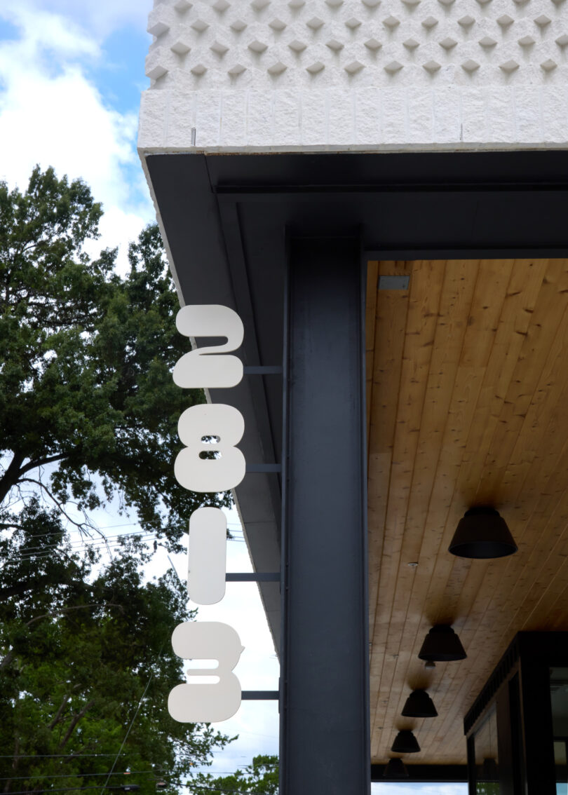 Modern building facade on Powell with large white numbers "2813" mounted vertically on a metal beam; features wood-paneled soffit and trees in the background.