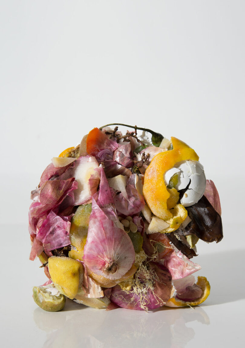 A pile of assorted food scraps, including citrus peels, onion skins, and vegetable remains, arranged against a plain white background.