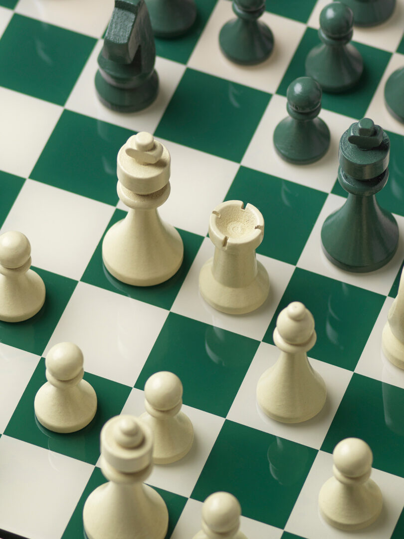 A chessboard with green and white squares shows chess pieces mid-game. White pieces are in the foreground; green pieces are in the background.