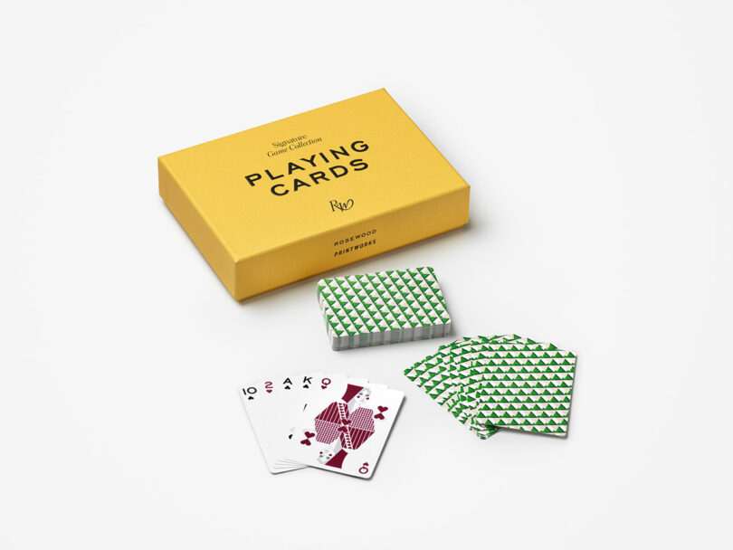 A yellow box labeled "Playing Cards" next to a deck of cards with green geometric backs and several face cards spread out on a white surface.