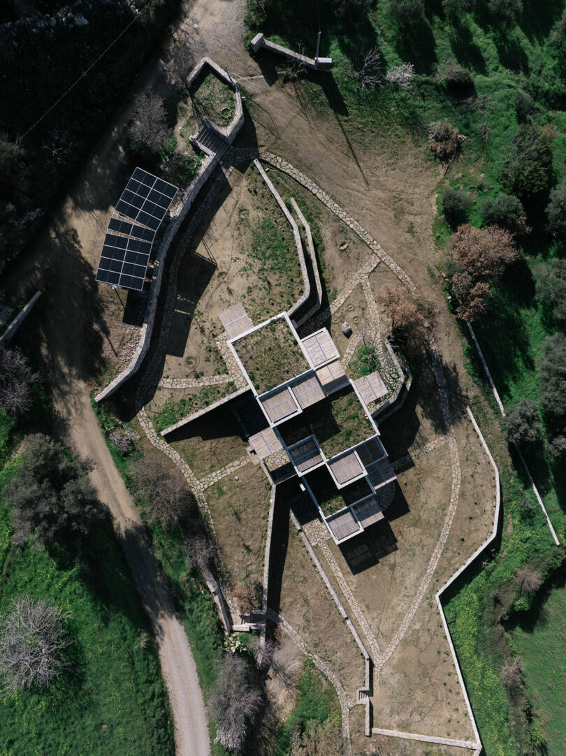Aerial view by Meraki Studios of a geometric, stone-walled structure with intersecting pathways, surrounded by grass, dirt paths, and trees.