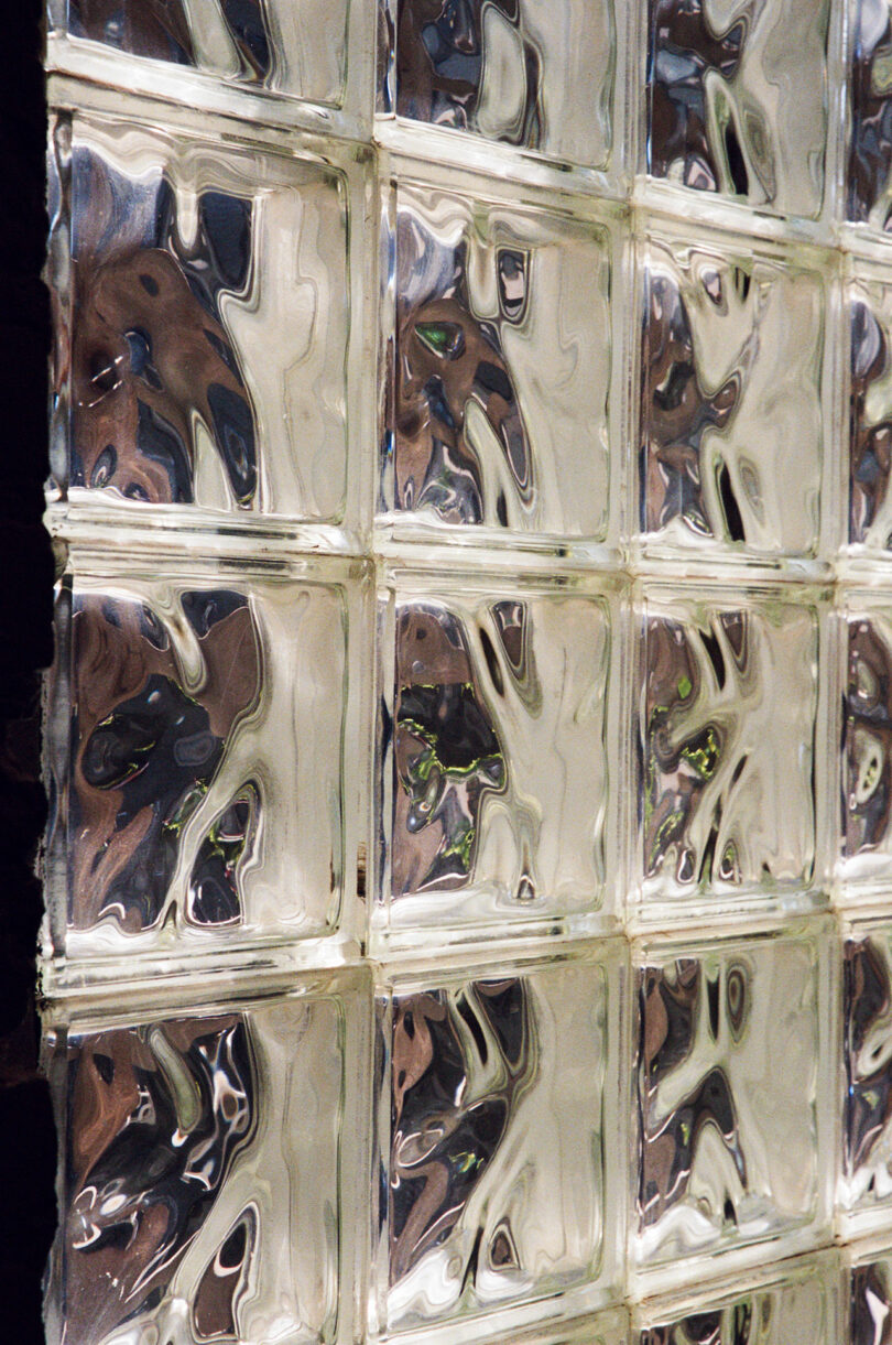 Close-up of a wall made of clear, wavy glass blocks arranged in a grid pattern, distorting light and images behind them.