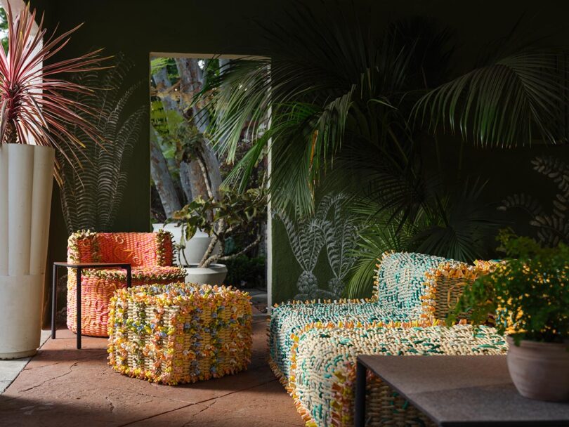 A sunlit room from The Future Perfect features colorful, textured woven furniture, potted plants, and an open doorway revealing greenery outside.