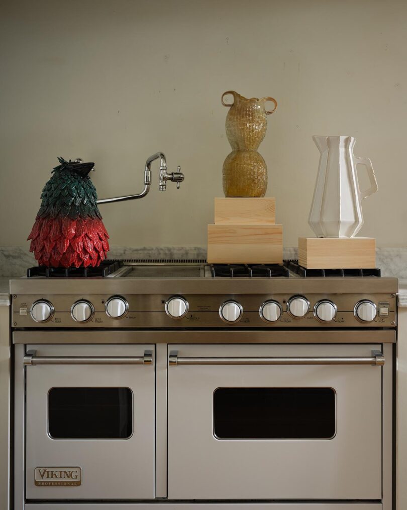 A stainless steel Viking oven with decorative objects, including a jug, a ceramic pitcher, and a sculptural vase from The Future Perfect, arranged on top.