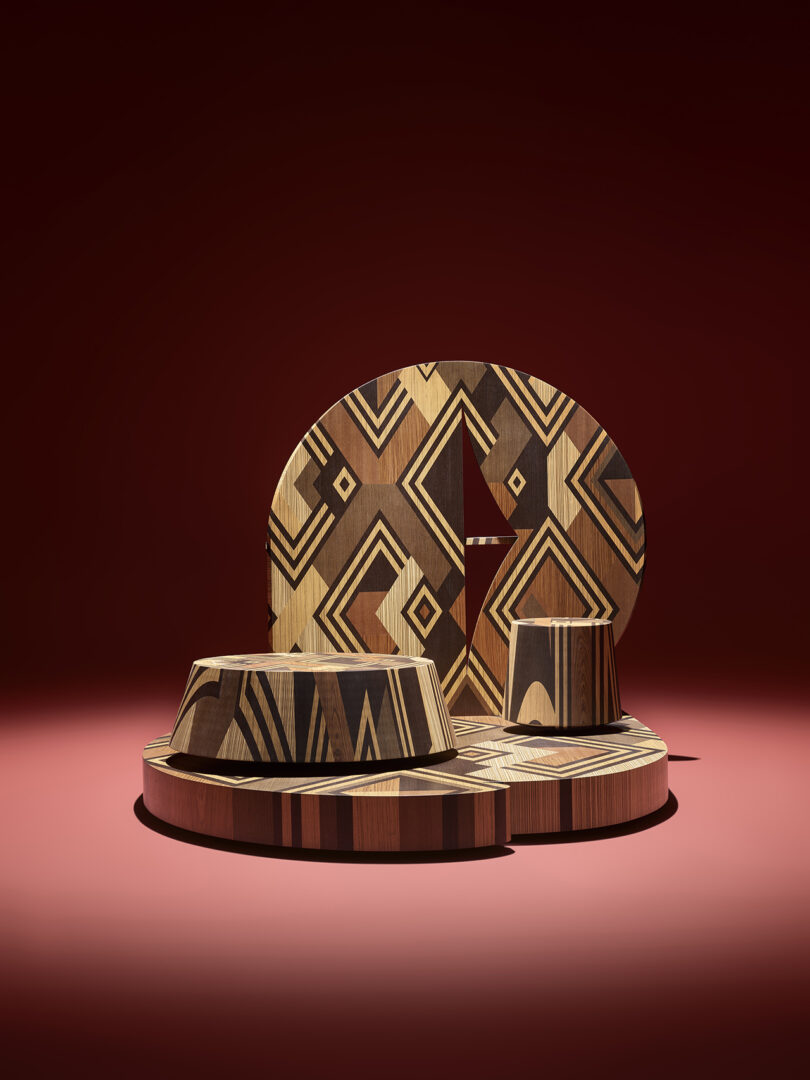 Geometric wooden platforms with intricate black patterns are arranged on a red surface against a dark red background.