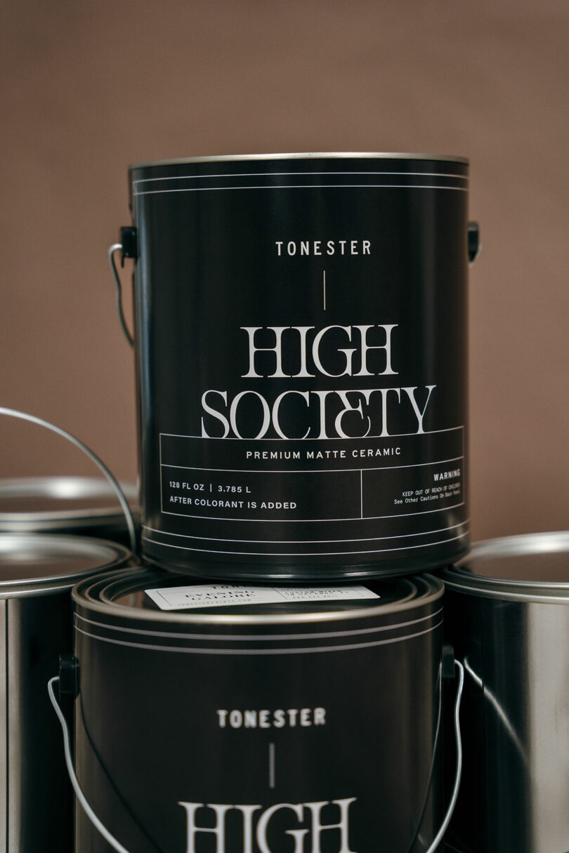 A close-up of three stacked black paint cans labeled "Tonester High Society Premium Matte Ceramic" against a brown background.