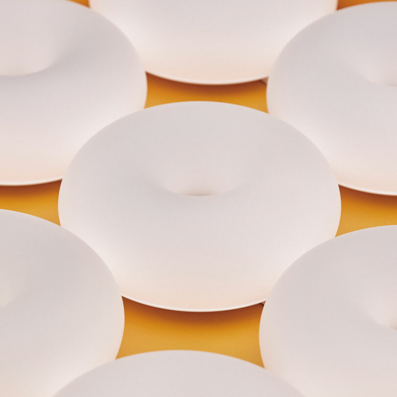 Rows of white, round objects with a hole in the center are arranged closely together on a yellow surface.
