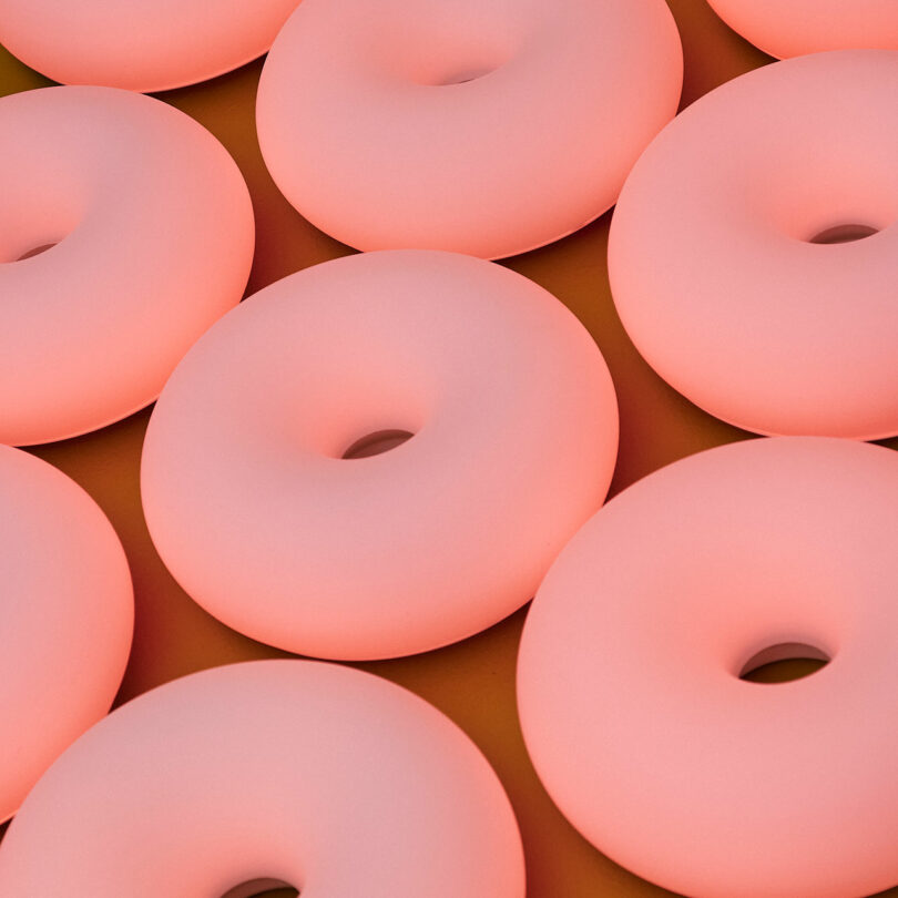Close-up view of several pink, smooth, donut-shaped objects arranged in a grid pattern on a brownish surface.