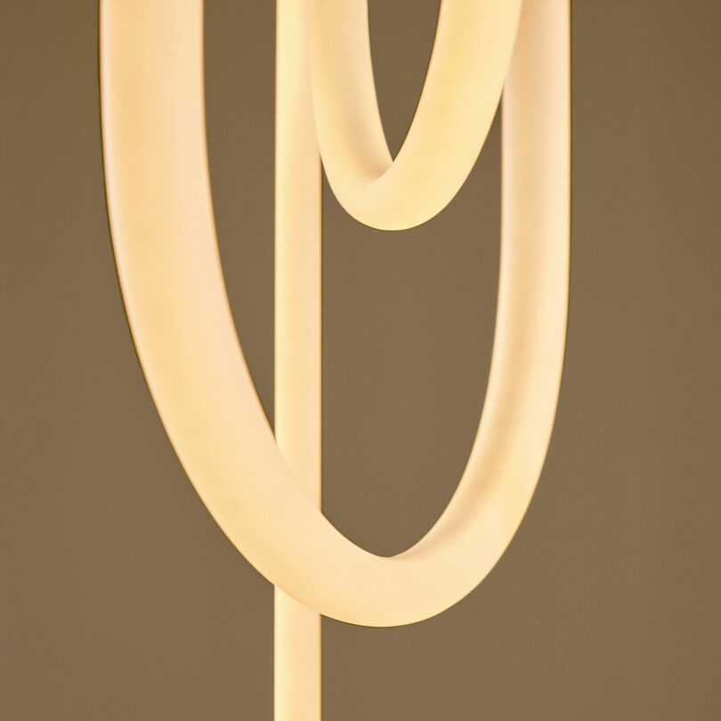 Close-up of two intersecting, curved, glowing light tubes against a neutral background.