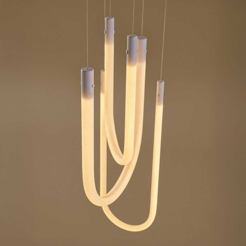 A modern pendant light fixture with four curved, glowing tubes hanging from the ceiling against a plain background.