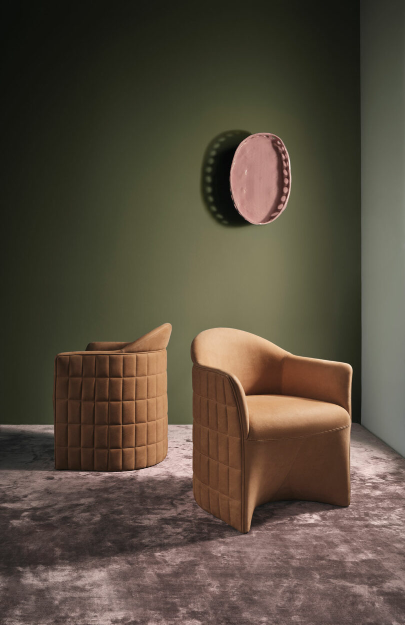 Two tan, quilted Wittmann chairs sit on a textured gray rug against an olive green wall, with round pink wall decor mounted above them.